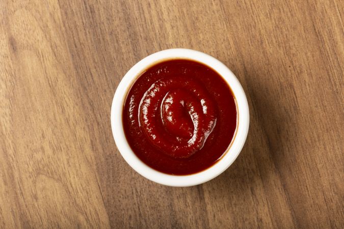 Tomato ketchup in the ramekin on wooden background.