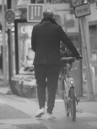 Back view of man walking with bike in grayscale