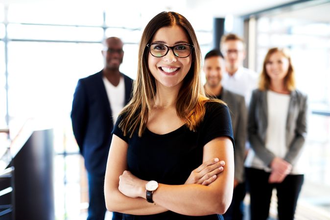 Smiling woman in glasses pictured in front of her colleagues in a bright office