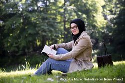 Smiling woman in headscarf sitting on the grass with a book 5z8pAb