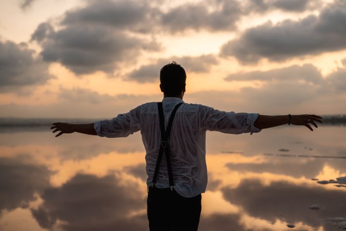 Relaxed man standing with outstretched hands with empty fish tank at shore