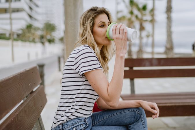 Happy woman with disposable cup of coffee sitting on street bench