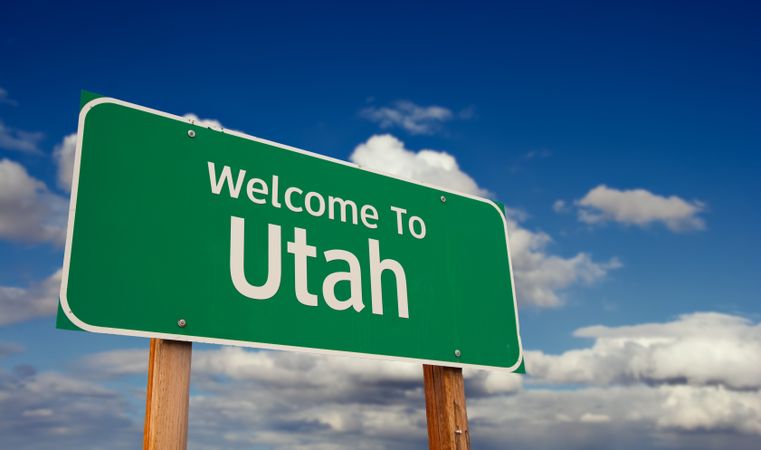 Welcome To Utah Green Road Sign Over Blue Sky with Some Clouds.