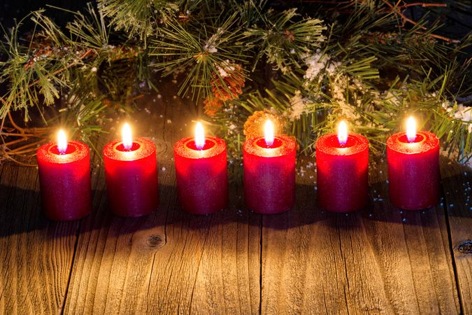 Glowing red candles with snow covered evergreen branch on wood