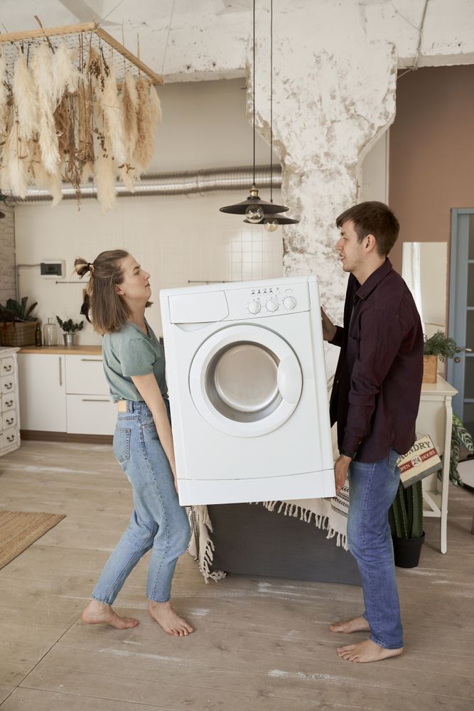 Enthusiastic couple carrying washing machine into new kitchen