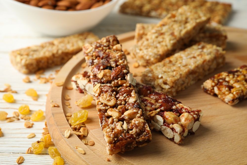 Tray with granola bars and bowl with almond on wooden background