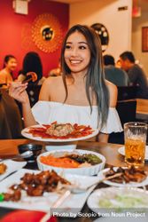 Smiling young woman eating asian food in restaurant 5kMQDb