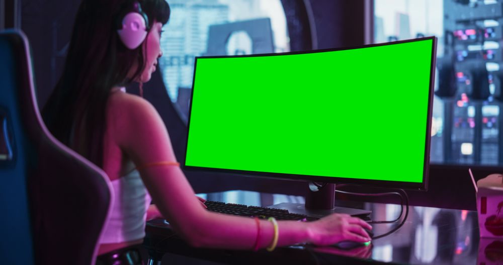 Over the Shoulder Footage of a Young Excited Gamer Playing a Video Game on a Desktop Computer with Green Screen Mock Up Display.