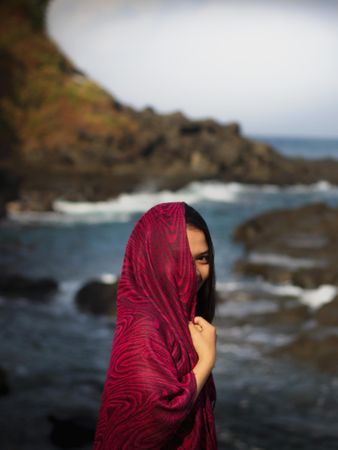 Woman covering her face standing on rock near body of water