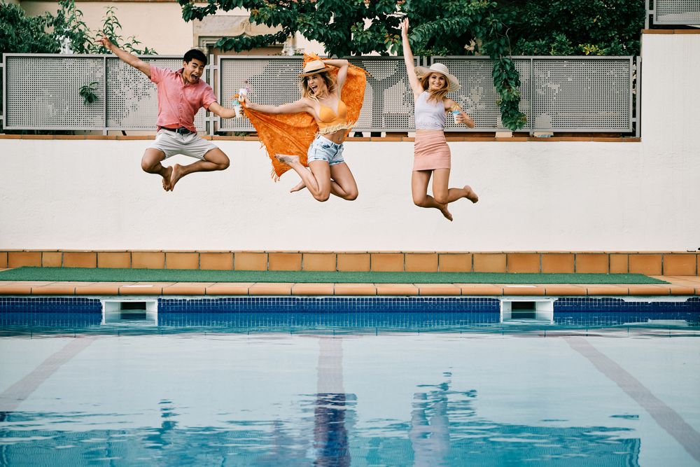 two young women and a man jumping by the pool