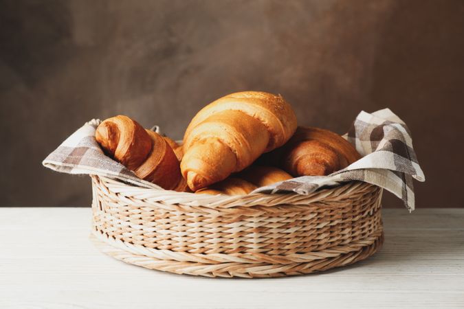 Wicker basket with croissants on table, space for text