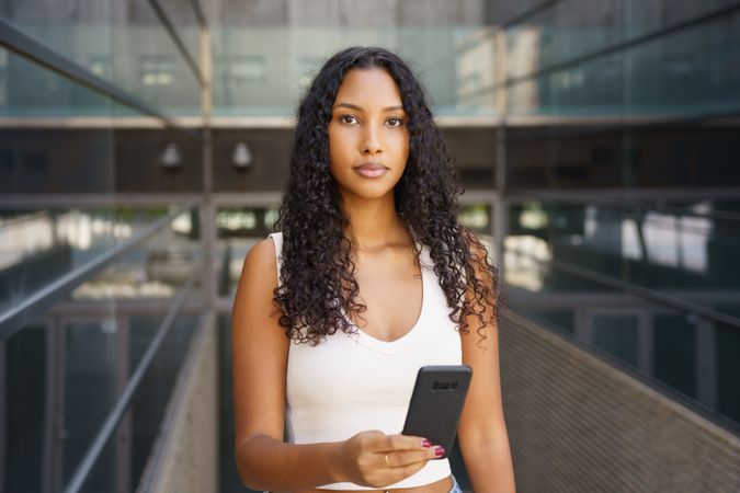 A confident young woman with a smartphone in a vibrant city, showcasing style and creativity
