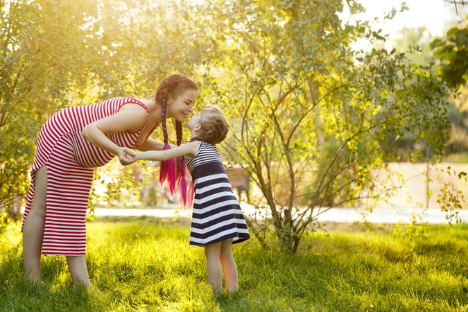 Pregnant woman reaching down to kiss her child in a sunny park