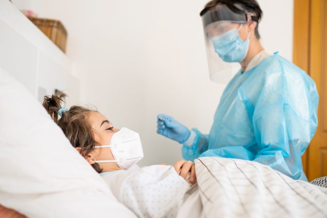 Child in facemask in hospital bed with medical professional caring for her