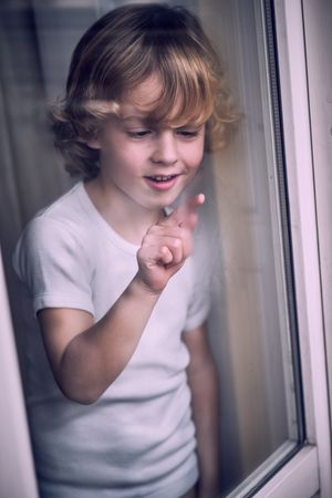 Happy little child drawing on misted window glass