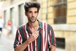 Portrait of serious dark haired man standing outside with hand on chest