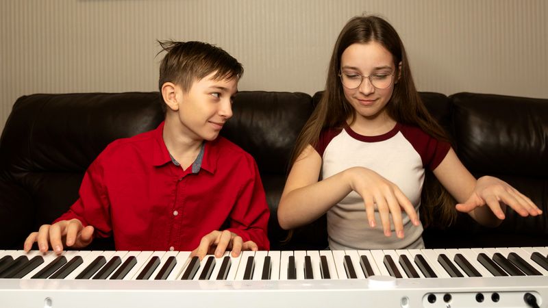 Boy playing the piano, smiling at girl beside him.