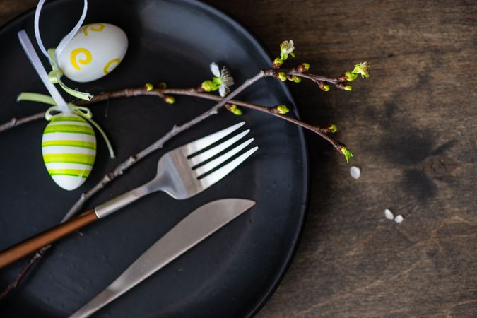 Table setting for Easter dinner with egg ornaments and branch on dark plate