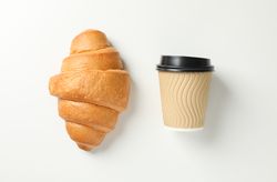 Flat lay of croissant and cup of coffee on plain background
