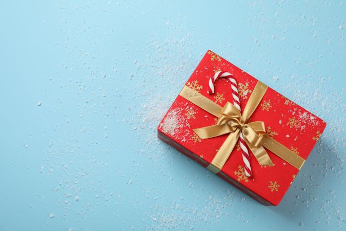 Gift box, candy cane and snow on blue background, top view