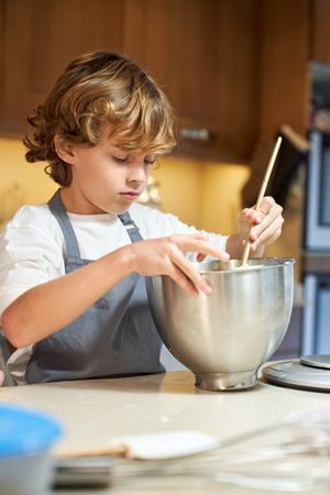 Vertical photo of a child mixing ingredients in a metal container