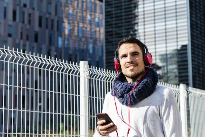 Young man listening to music on headphones while holding a mobile phone outdoor