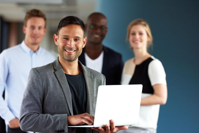 Business man holding small laptop and smiling in front of his colleagues