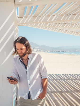 Relaxed man using smartphone in gazebo on beach