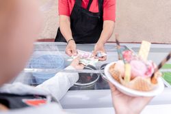 A young Hispanic woman is waiting for her change while holding a big traditional Mexican ice cream
