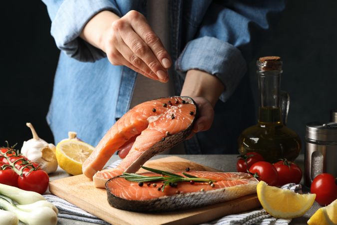 Woman sprinkles salt on salmon meat. Cooking salmon on gray table