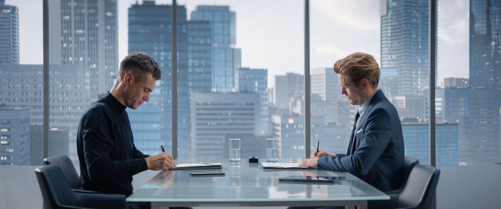 Two Businessmen Sitting in Skyscraper Office and Signing Profitable Contract.