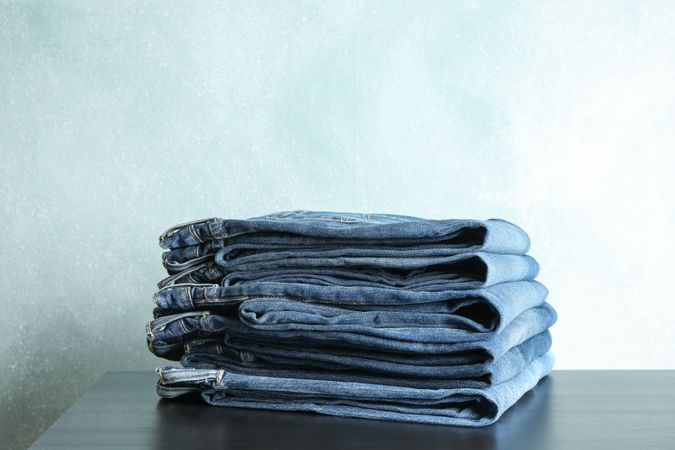 Stack of jeans pants on table, space for text