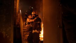 Brave fireman descends stairs of a burning building with a saved girl in his arms.