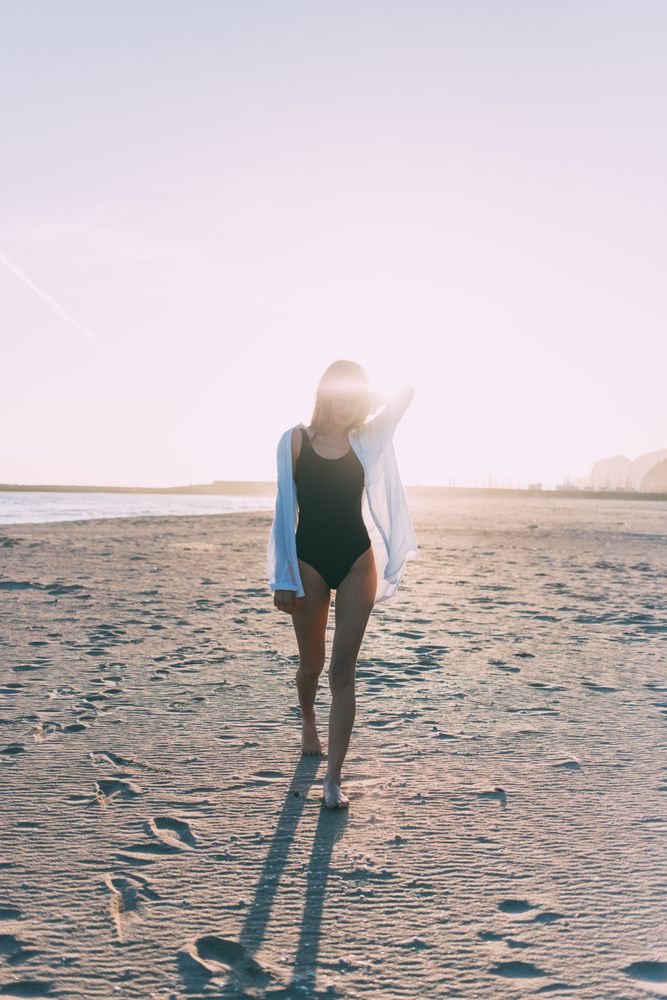 Female standing on beach with sunset at her back with bright sun