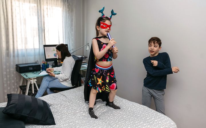 Children playing and dancing on the bed while their mother works in pajamas at home