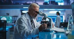 Medical Development Laboratory: White Male Scientist Using Microscope, Analyzes Petri Dish Sample.