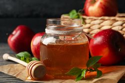 Pot of honey with dipper in front of basket of apples