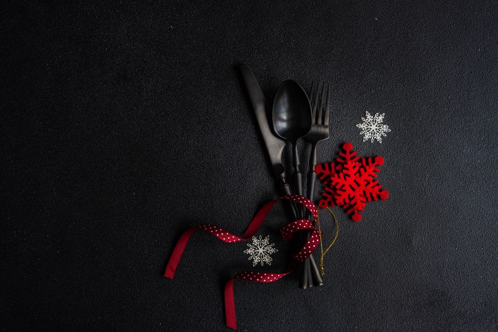 Dark cutlery on dark background tied with festive red ribbon and snow flake ornament