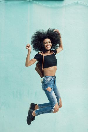 Female in casual clothes jumping for joy while raising her arms in celebration