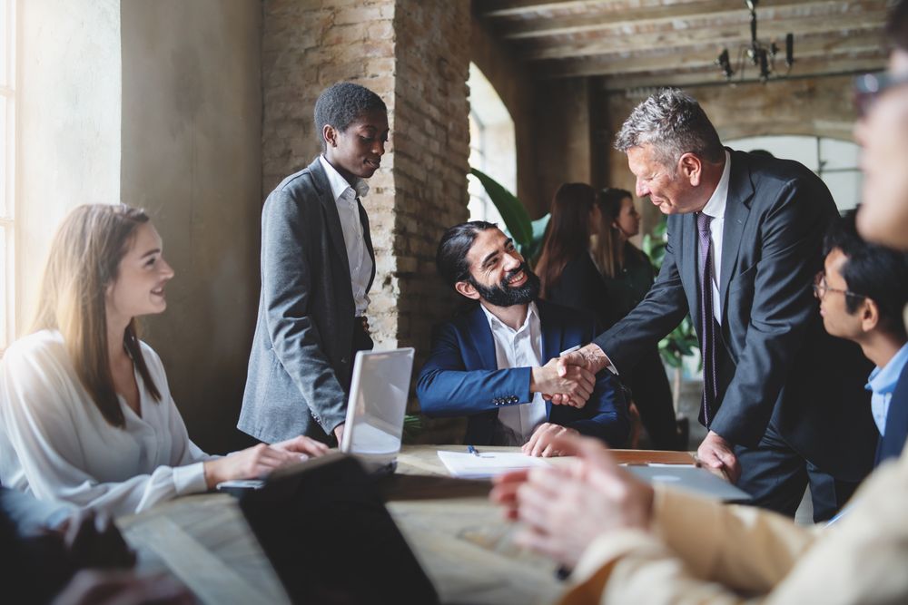 Two businessmen make a deal by shaking hands sitting at a table together