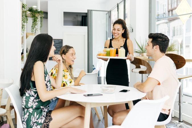 Cheerful waitress serving healthy drinks for friends