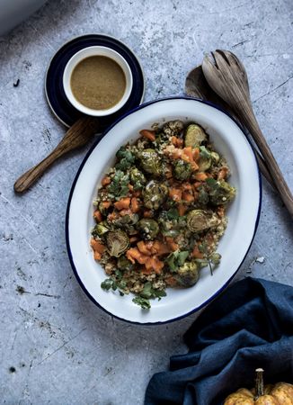 Braised brussels sprouts and pumpkin with quinoa in bowl near cup of sauce