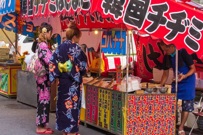 Two women in kimonos standing at a food kiosk in Kyoto, Japan