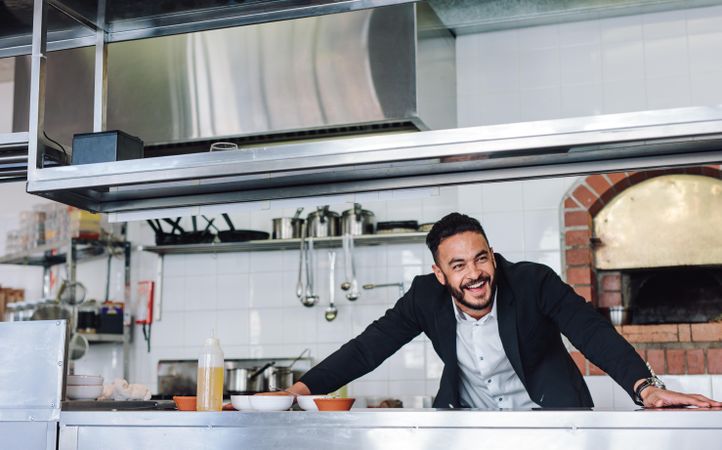 Happy young restaurant owner standing at kitchen counter looking away and smiling
