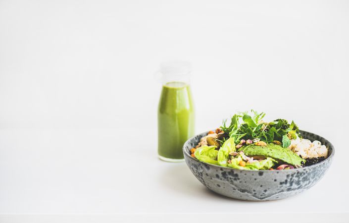 Healthy vegetarian bowl pictured on light background with smoothie on side, copy space