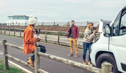 Woman in woolen sweater working on car engine while partner makes emergency call