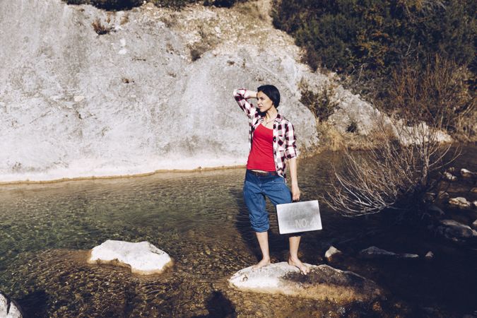 woman standing on rock with case near clear water in lake