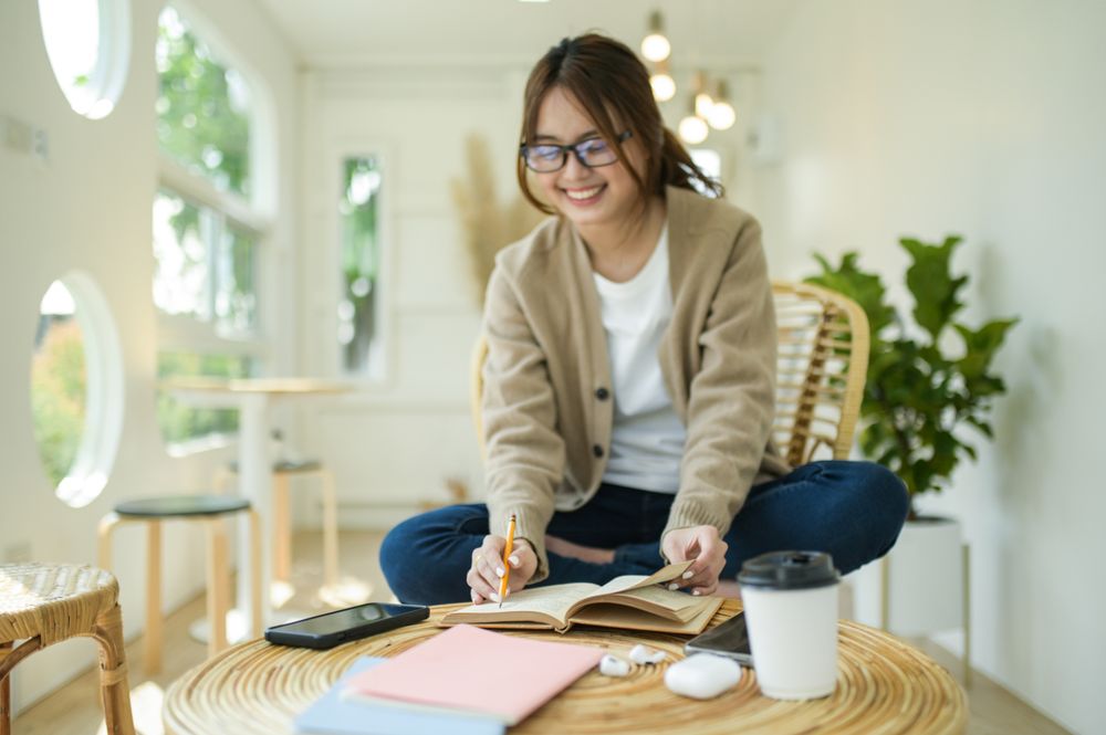 A young woman reading a book and sitting in a comfortable chair at home.