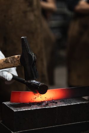 Blacksmith in gloves hot hitting metal part on anvil