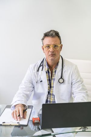 Male doctor working in medical office while looking at camera. Vertical shot